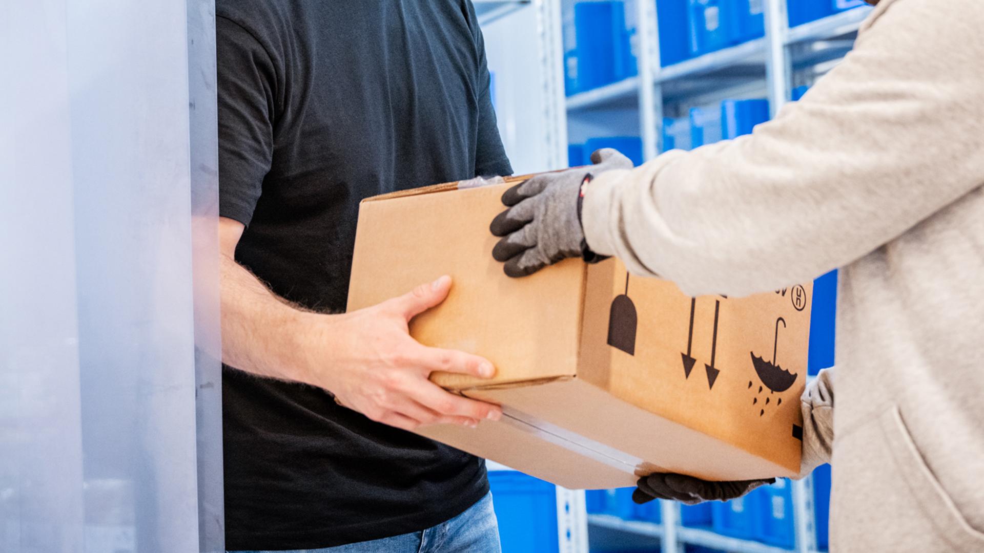 Zwei Personen übergeben sich ein Paket; eine Person trägt Handschuhe